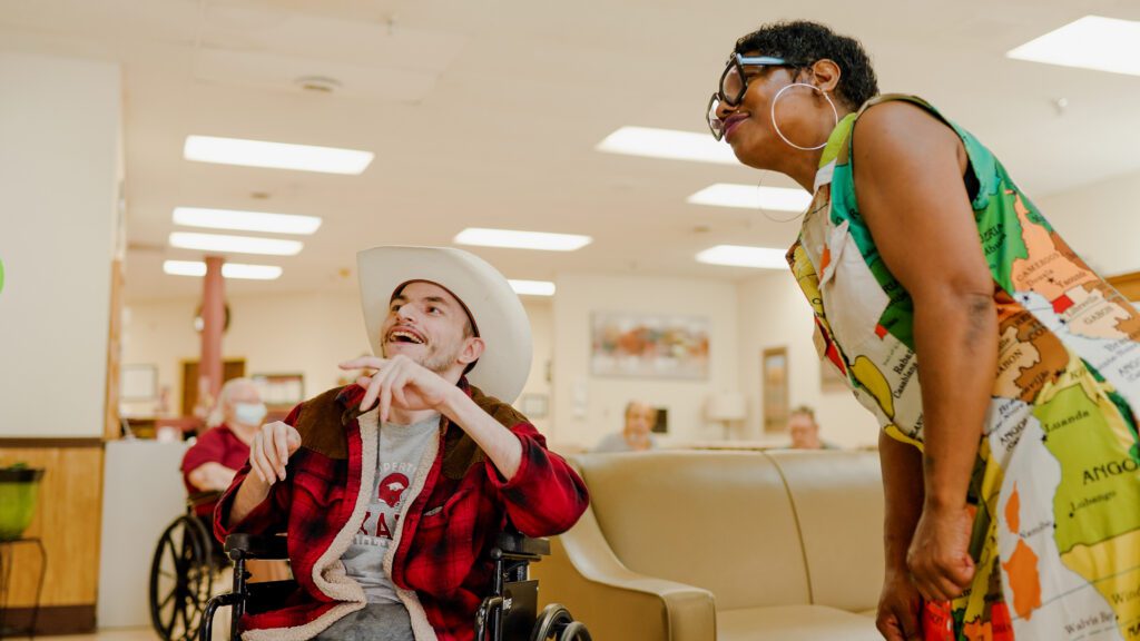 A man in a wheel chair and a Bailey Creek staff member smiling at a skilled nursing facility